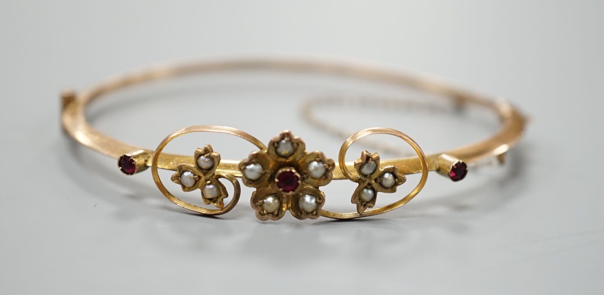 An Edwardian 9ct, red stone and seed pearl set hinged bangle, interior diameter 55mm, gross weight 4.4 grams.